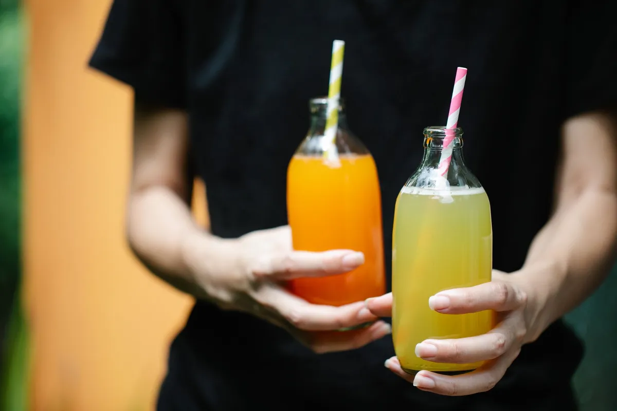 Two colorful juices in glass bottles with straws, perfect for summer refreshment.